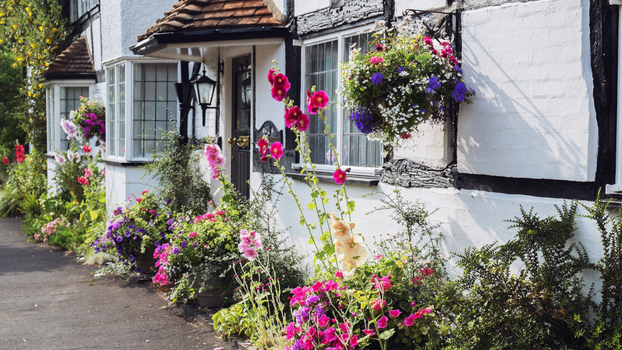 Airbnb listing photo example of a charming cottage exterior with colorful flower garden and hanging baskets
