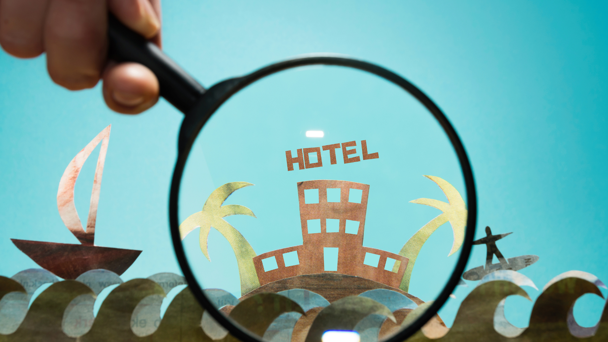 Magnifying glass highlighting a cardboard hotel, symbolizing how Jurny’s AI-powered reservation system prevents double bookings with real-time sync.